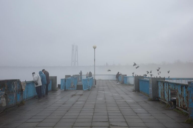 Люди стоять на туманній набережній річки. Фото: Elena Tita