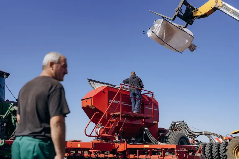Працівники агрофірми завантажують сівалку Horsch із великого білого мішка, підвішеного на навантажувачі. Фото: Софія Соляр.
